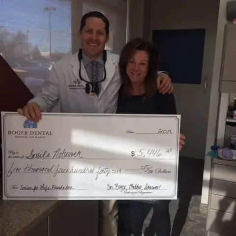 Smile a man and woman dentist holding a large check | Boger Dental | Plymouth, MN